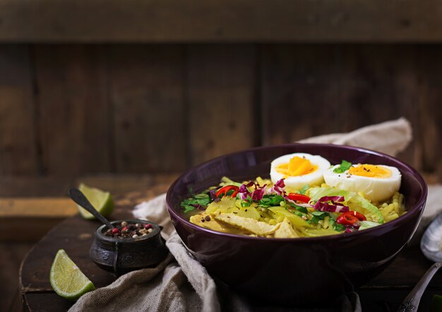 Sopa de macarrão com frango, aipo e ovo em uma tigela sobre uma mesa de madeira velha.