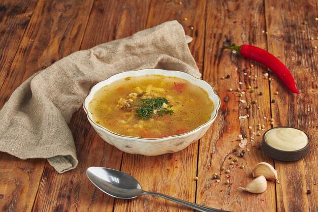 Sopa de macarrão em uma tigela, colher na mesa de madeira