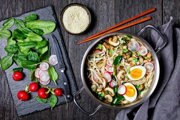 Sopa de macarrão udon, prato asiático de caldo kakejiru à base de dashi, molho de soja e mirin com espinafre, rabanete, ovos cozidos moles, cogumelos fatiados servidos em uma panela com pauzinhos e ingredientes, vista superior,