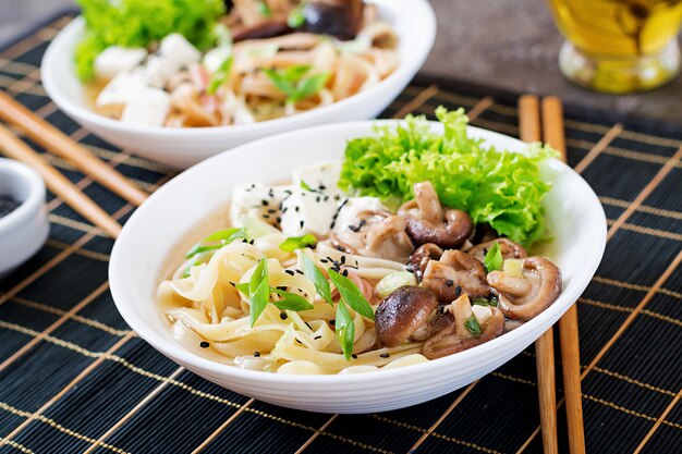 Sopa de macarrão vegan com queijo tofu, cogumelos shiitake e alface em uma tigela branca. comida asiática.