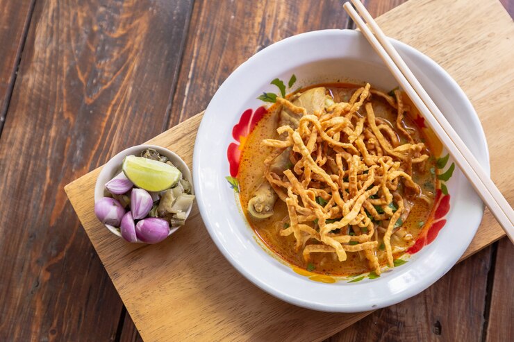 Sopa de macarronete surrada (soi de Khao) com carne da galinha e leite de coco picante na tabela de madeira.