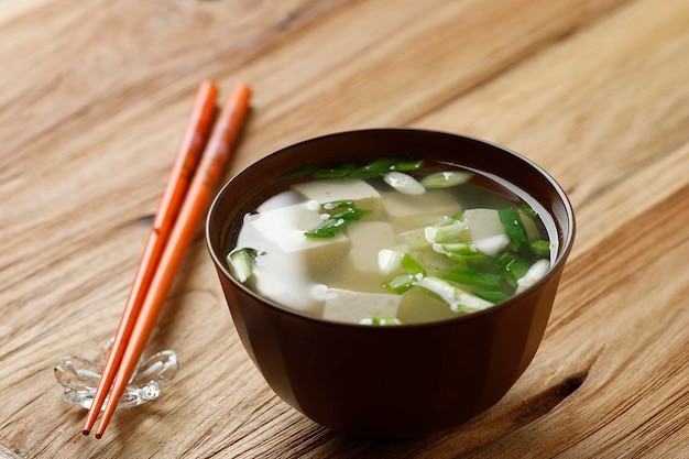 Sopa de missô japonesa com cebolinha e tofu em cubos em uma mesa de madeira de tigela marrom