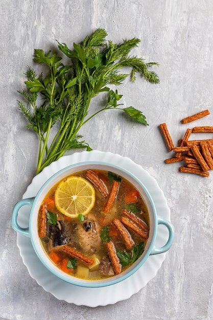 Sopa de peixe com batatas e cenouras, sobre um fundo de concreto com uma fatia de limão, ervas e bolachas