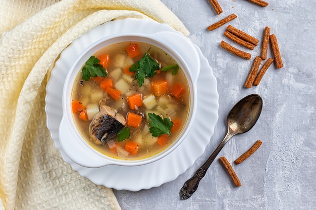 Sopa de peixe com batatas e cenouras, sobre um fundo de concreto com verduras e biscoitos