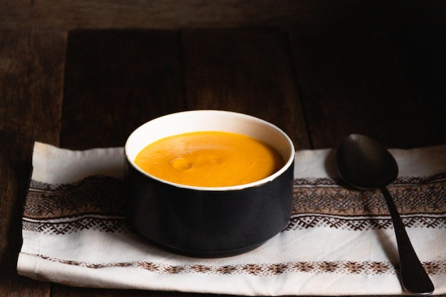 Sopa de purê de abóbora em uma tigela de cerâmica sobre uma mesa de madeira com um guardanapo de cozinha folclore.