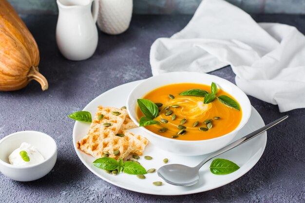 Sopa de purê de abóbora pronta para comer com sementes de abóbora, folhas de manjericão e torradas em um prato sobre a mesa. Comida vegetariana. Dia de ação de graças