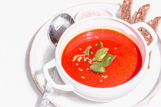 Sopa de purê vermelho com tomate, verduras e pão. Luz dura na moda, sombra escura. Fundo de massa branca, close-up