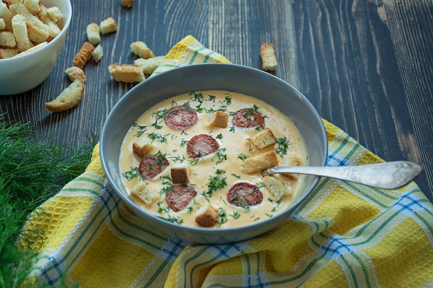 Sopa de queijo com salsichas grelhadas e ervas. Sopa de creme servida em um prato.