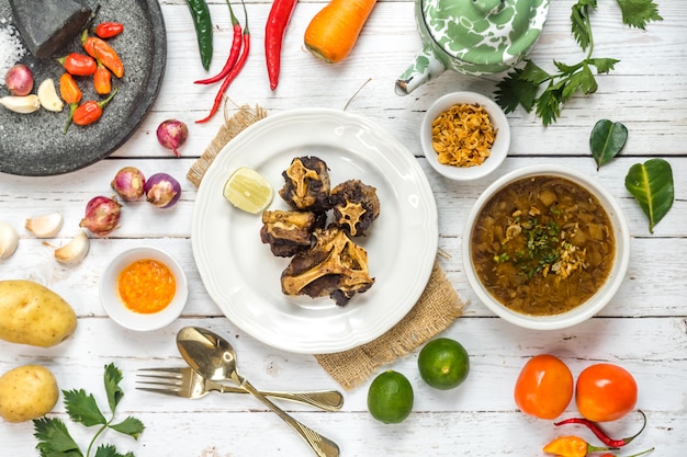 Sopa de rabo de boi e rabo de boi frito são servidos na mesa lado a lado com os temperos básicos