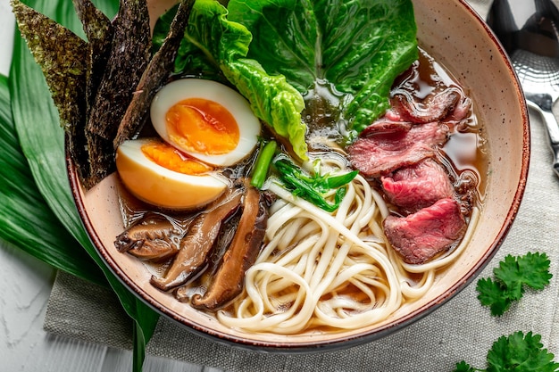 Sopa de ramen asiática com cogumelos de macarrão de arroz e carne de porco em tigela preta Cozinha asiática