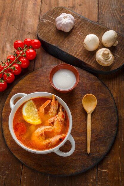 Sopa de tom inhame com camarão e leite de coco na mesa em uma placa redonda ao lado de leite de coco e tomate.