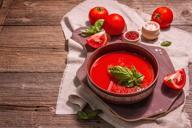 Sopa de tomate com manjericão em uma tigela. Legumes maduros, verduras frescas, especiarias aromáticas. Mesa de madeira vintage, cópia espaço