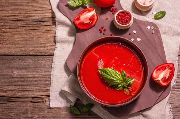 Sopa de tomate com manjericão em uma tigela. Legumes maduros, verduras frescas, especiarias aromáticas. Mesa de madeira vintage, vista superior