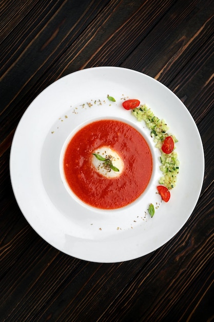 Sopa de tomate em um prato branco sobre um fundo de madeira
