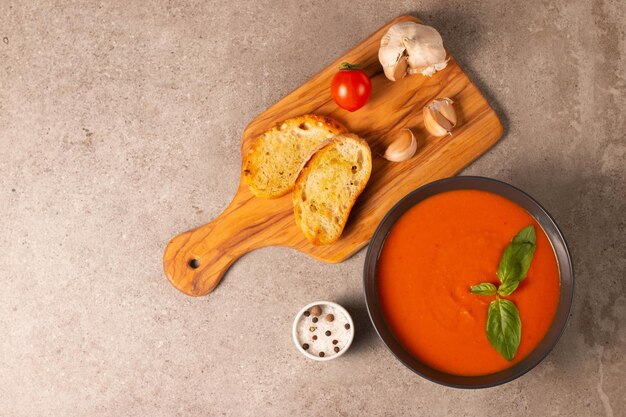 Sopa de tomate fresca e saudável com manjericão pimenta alho tomate e pão em fundo de madeira