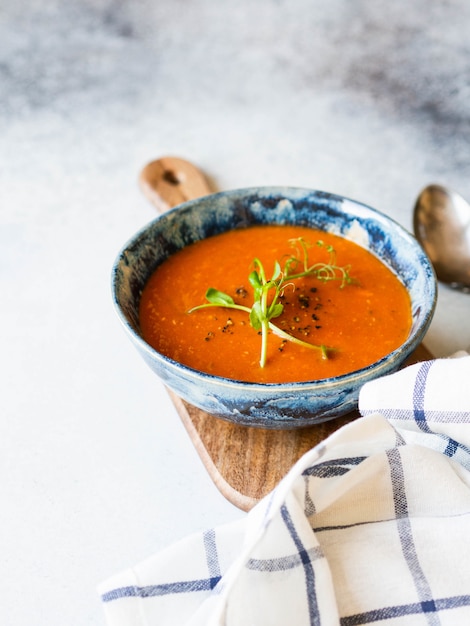 Sopa de tomate fresco com especiarias e brotos de ervilha fresca em tigela rústica azul na placa de madeira na luz