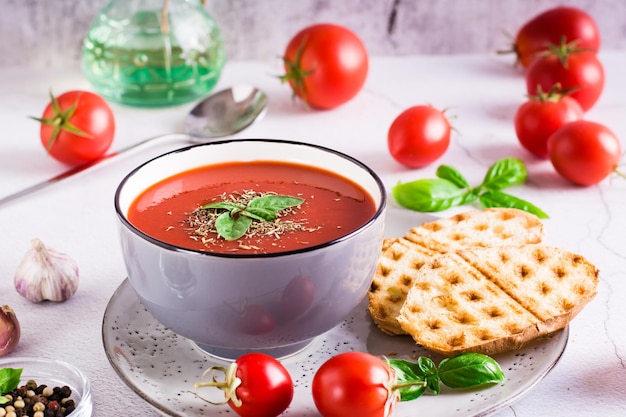 Sopa de tomate fresco com manjericão em uma tigela e legumes frescos na mesa