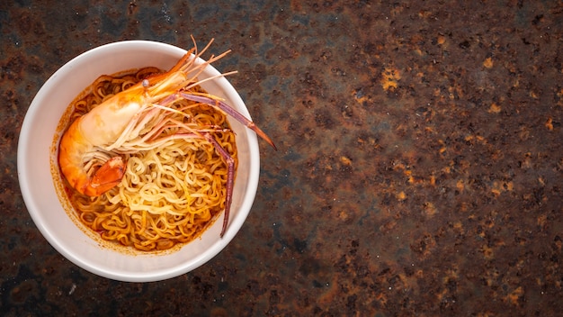 Sopa de fideos agridulce con camarones en cuenco de cerámica blanca sobre fondo de textura oxidada, vista superior, langostinos de río, Tom Yum Goong, Tom Yum Kung, comida tailandesa