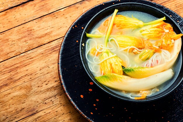 Foto sopa con fideos de arroz y flores de calabaza. sopa vegana asiática.