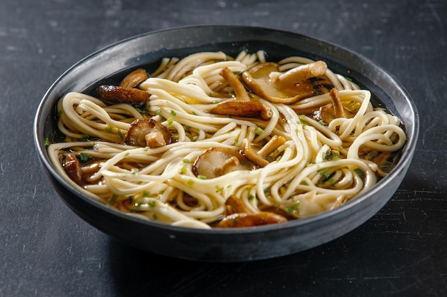 Sopa de fideos asiáticos con shiitake de setas servida en un tazón oscuro. De cerca