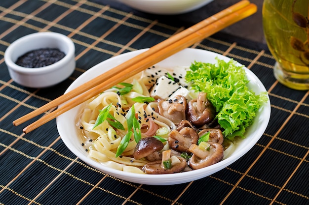 Foto sopa de fideos veganos con queso de soja, champiñones shiitake y lechuga en un tazón blanco. comida asiática.