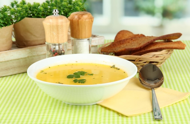 Sopa fragante en plato blanco sobre mantel verde en primer plano de fondo de ventana