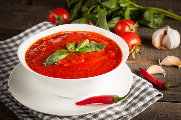 Sopa fresca, sana del tomate con albahaca, tomates en fondo de madera. Sopa de gazpacho español.