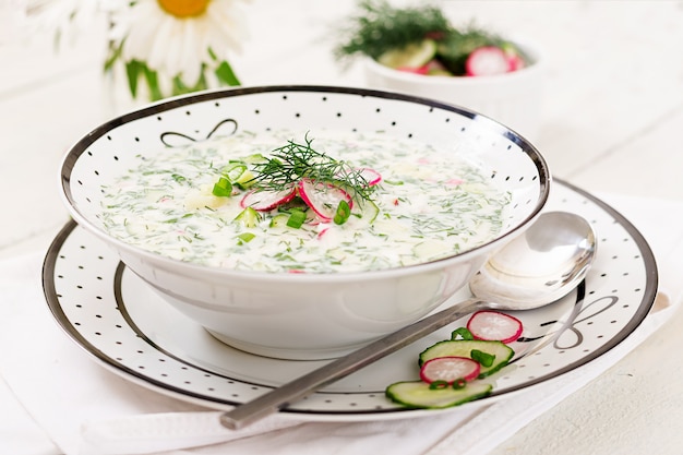 Sopa fria com pepinos frescos, rabanetes com iogurte em uma tigela na mesa de madeira.