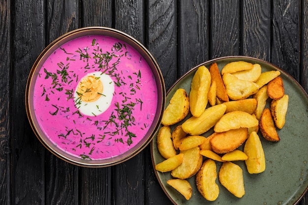 Sopa fria de borscht com ovo cozido e fatias de batata frita para enfeitar a mesa de madeira, um tiro de cima