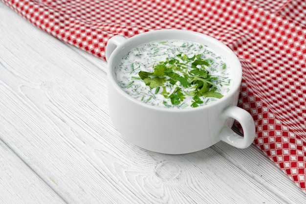 Sopa fría de verano ruso Okroshka sobre mesa de madera blanca con servilleta