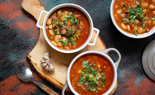 Sopa de frijoles con carne y verduras servida sobre una tabla rústica con ajo. Sopa o guiso tradicional de los Balcanes Corbast Pasulj (Grah). Vista superior, espacio de copia