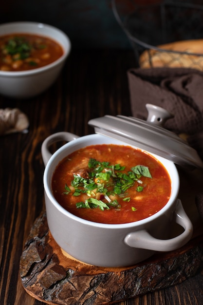 Sopa de frijoles con carne y verduras servida sobre una tabla rústica y mesa de madera con pan y ajo. Sopa tradicional de los Balcanes Pasulj (Grah). Primer plano, enfoque selectivo