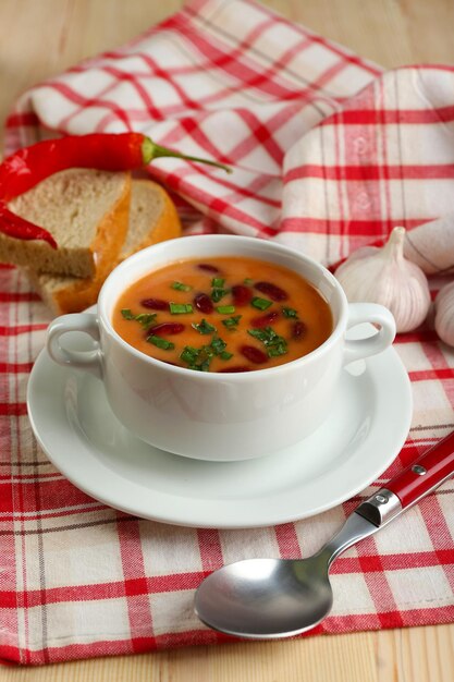 Foto sopa de frijoles en un tazón con pan fresco en rodajas en una servilleta sobre fondo de mesa de madera