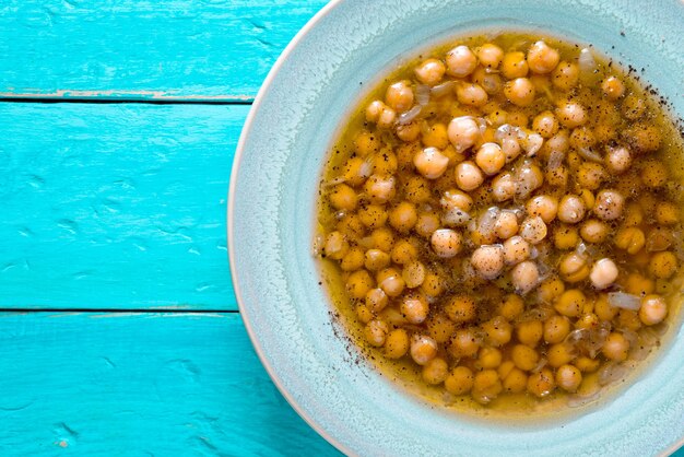 Foto sopa de garbanzo griego en el plato blanco sobre el fondo cian vista superior vertical