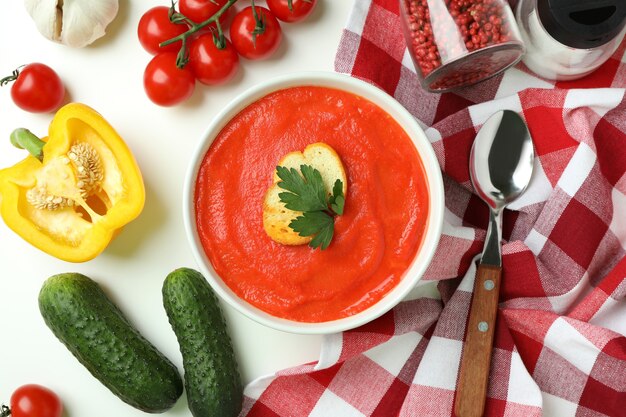 Sopa de gazpacho e ingredientes sobre fondo blanco.