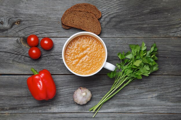 Sopa de gazpacho e ingredientes sobre superficie de madera oscura.