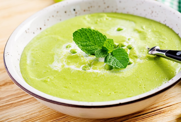 Sopa de guisantes verdes en un recipiente en la mesa de madera