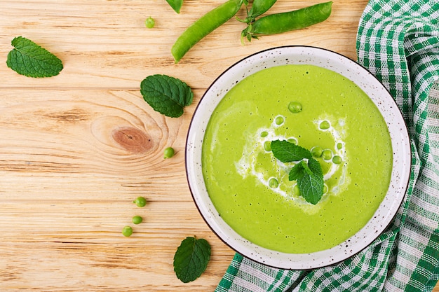 Sopa de guisantes verdes en un tazón sobre la mesa de madera, cocina francesa, vista superior