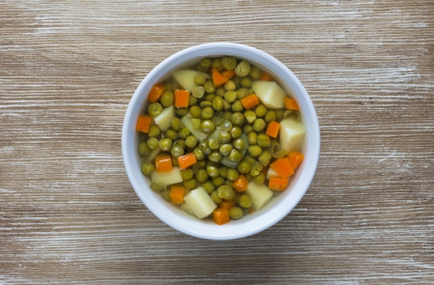 Sopa con guisantes y verduras en un tazón blanco sobre fondo de madera