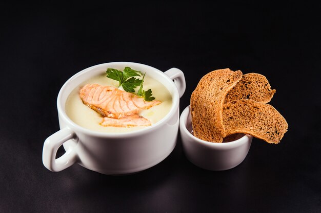 Sopa de leche con salmón y galletas saladas sobre fondo negro