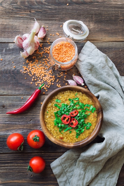 Sopa de lentejas casera en un tazón con ingredientes sobre fondo de madera rústica. Comida vegetariana saludable.