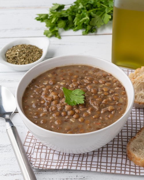 Sopa de lentejas marrones en un bol con rebanadas de pan y condimentos sobre una mesa de madera