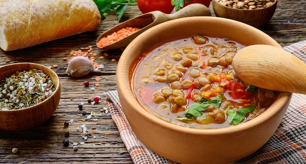 Sopa de lentejas en un tazón de madera con verduras y pan casero sobre la mesa de madera rústica.