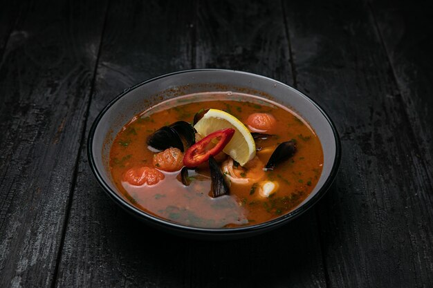 Sopa de mariscos con mariscos y salsas en una mesa de madera oscura.