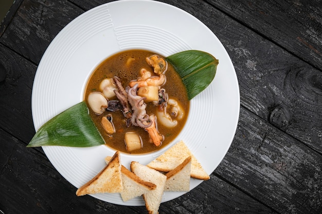 Sopa de mariscos con mariscos y salsas en una mesa de madera oscura.