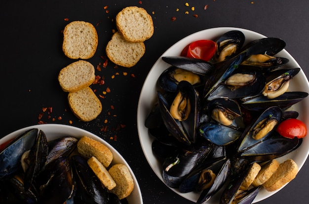 Sopa de mejillones al vapor con vino, pimientos picantes y pan crujiente sobre fondo negro. Mariscos italianos. Lay Flat, vista superior, espacio de copia