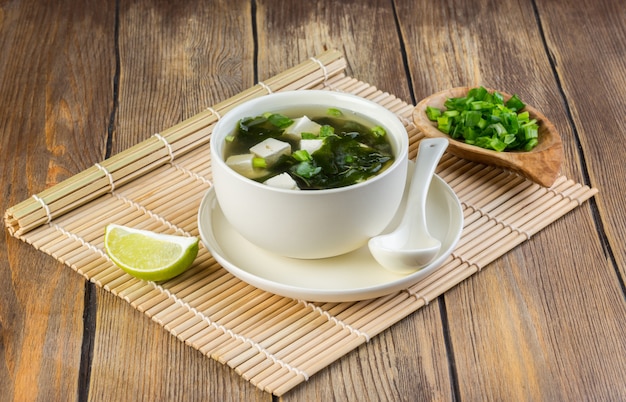 Sopa de miso japonesa en un cuenco blanco en la tabla cubierta con la estera de bambú. Copia espacio