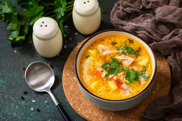 Sopa noruega con crema y salmón sobre una mesa rústica de madera sobre un fondo de piedra oscura