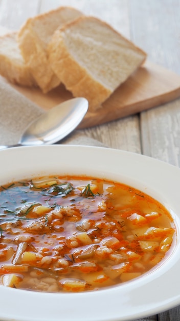 Sopa con patatas y cebada en un plato blanco y pan sobre una tabla para cortar