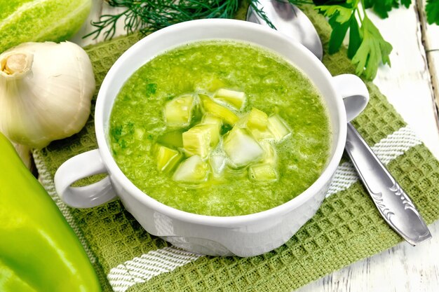 Sopa de pepino con pimientos verdes y ajo en un bol sobre una servilleta verde, perejil en las tablas de madera clara de fondo